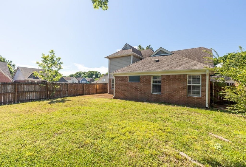 Fenced backyard featuring an expansive lawn, brick-clad exterior, and a multi-level roofline