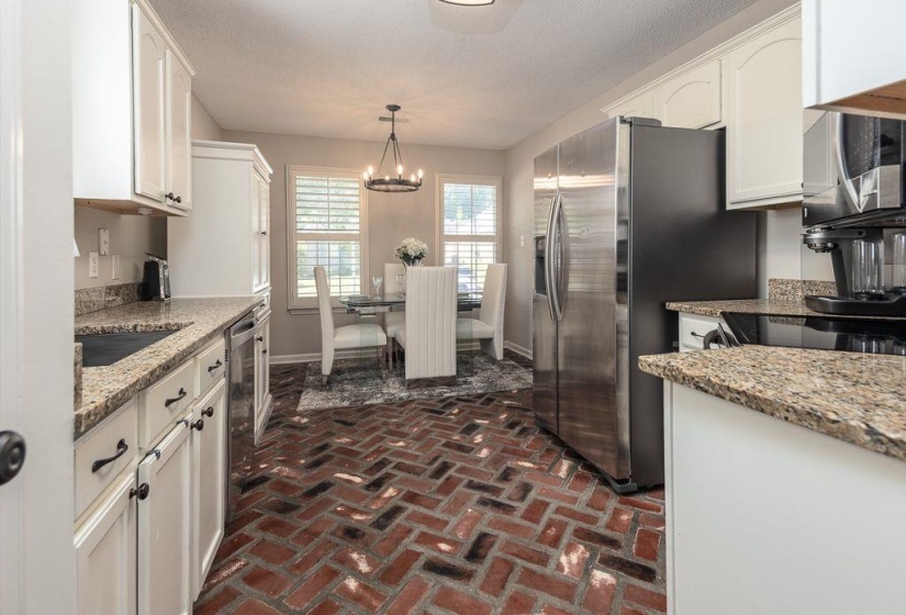 Kitchen featuring brick-pattern flooring, white cabinetry with dark hardware, stone-finish countertops, and stainless steel appliances