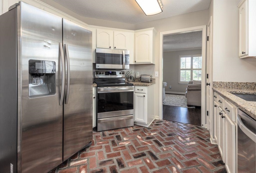 Kitchen featuring brick flooring, stainless steel appliances, white cabinetry, and stone countertops