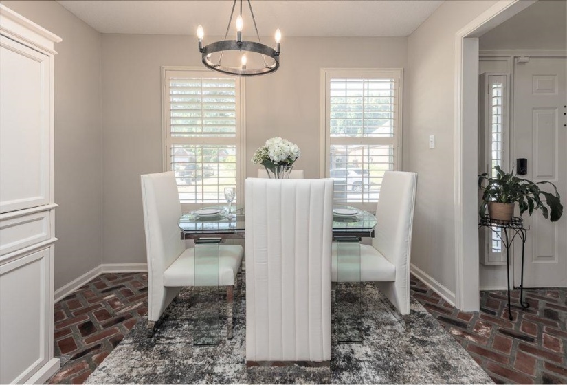 Dining area featuring brick flooring, plantation shutters, and a chandelier