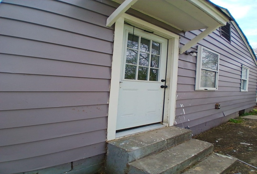 Exterior entry with a white paneled door featuring a multi-pane glass insert, protected by a small awning