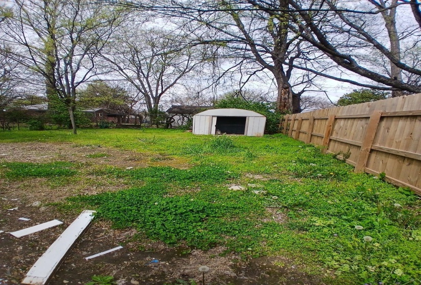 Expansive backyard featuring a wood privacy fence, mature trees, and a freestanding storage shed