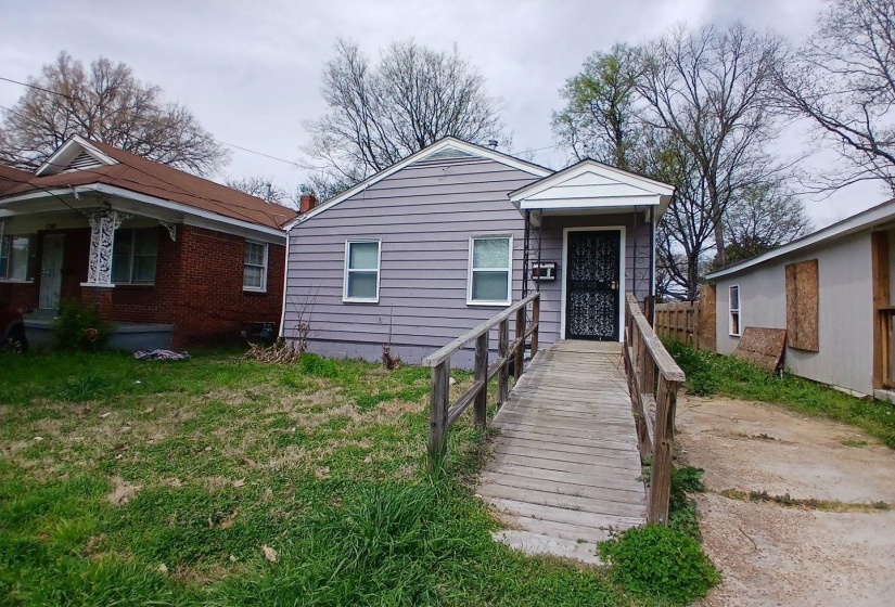 Single-story residence featuring light gray siding, white trim, a covered entry porch, a dark security screen door, and an exterior access ramp