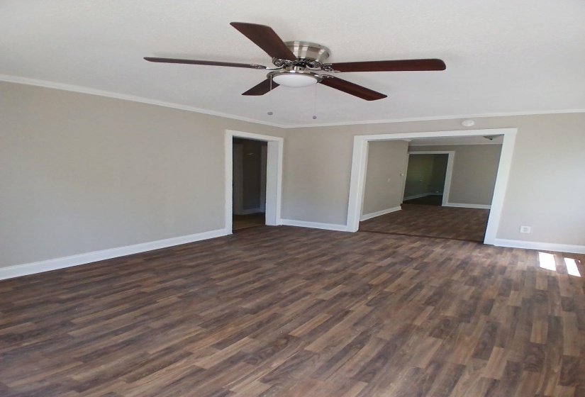 Spacious room featuring wood-finish flooring, neutral-toned walls, white trim, and a ceiling fan with integrated lighting