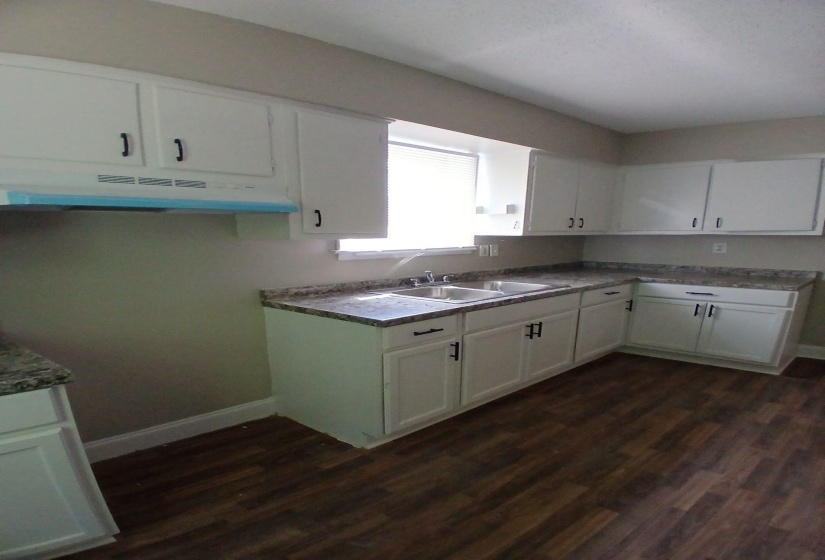 Kitchen featuring white cabinetry with dark hardware, a double-basin stainless steel sink, wood-finish flooring, and a light-colored countertop