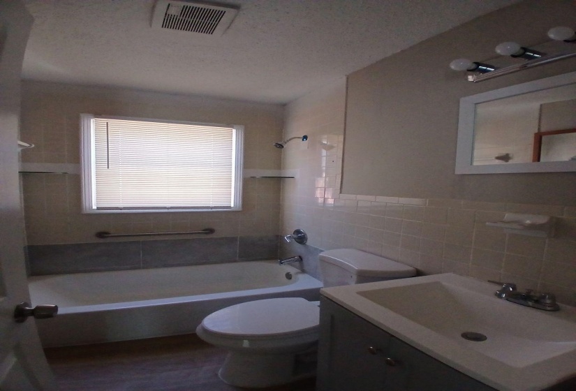Full bathroom featuring a tub/shower combination with tile surround, a built-in window with blinds, a toilet, and a vanity with an integrated sink