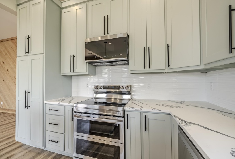 Modern kitchen featuring light-toned cabinetry with black hardware, stainless steel appliances, white subway tile backsplash, and elegant marble-patterned countertops