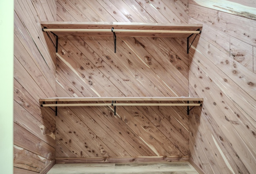Wardrobe space featuring diagonal wood paneling, two levels of shelving, and integrated hanging rods