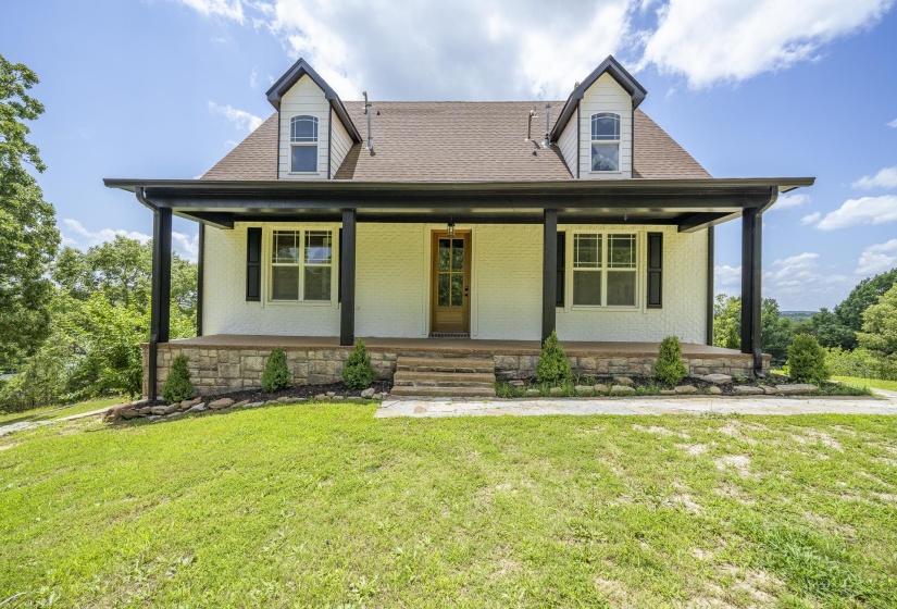 White brick facade featuring a covered porch with dark columns, a gabled roof, and two dormer windows