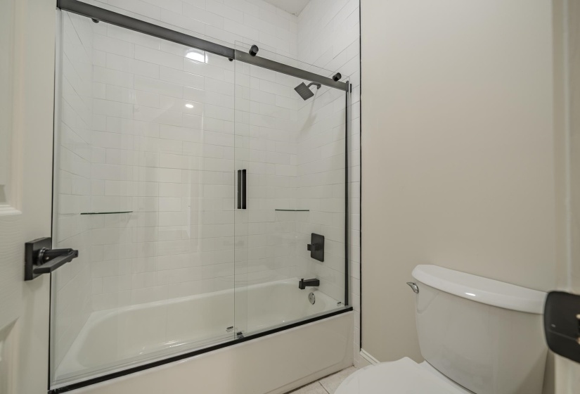 Bathroom featuring a white subway tile surround, a built-in bathtub, and a glass sliding shower door with matte black hardware