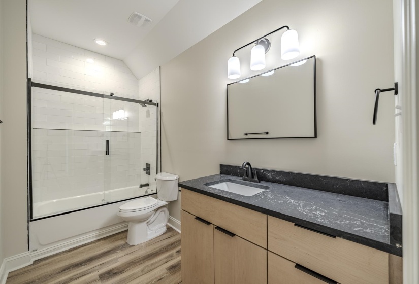 Bathroom featuring a vanity with a dark stone-look countertop, wood-finish cabinetry, and a rectangular undermount sink with a matte black faucet