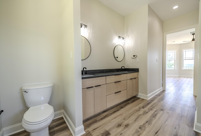 Dual vanity with light wood-finish cabinetry, dark countertops, and matte black fixtures