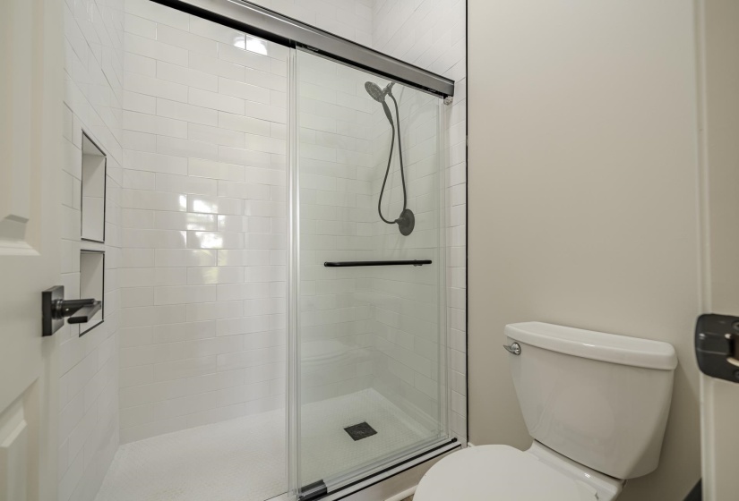 Contemporary shower with subway tile surround and integrated shelving, featuring a glass sliding door with black trim and hardware