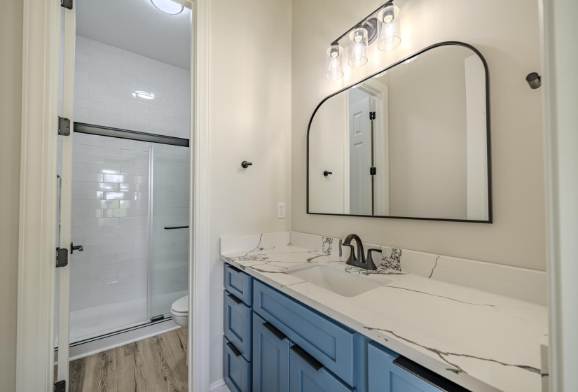 Bathroom featuring a blue vanity with a white countertop, an arched mirror, and a walk-in shower with white subway tile