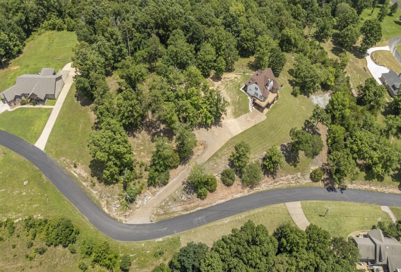 Aerial perspective showcasing a property surrounded by mature trees, featuring a paved roadway and a concrete driveway