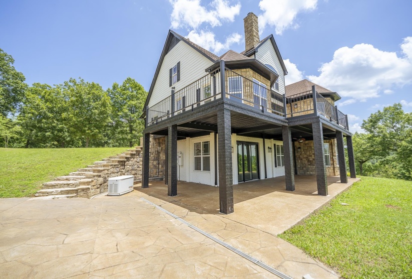 Multi-level residence featuring a stone and siding exterior, expansive upper decks with black railings, and a lower-level patio with stamped concrete