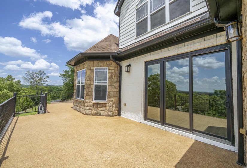 Spacious outdoor deck featuring an expansive concrete surface, black metal railing, and a stone-clad bay window