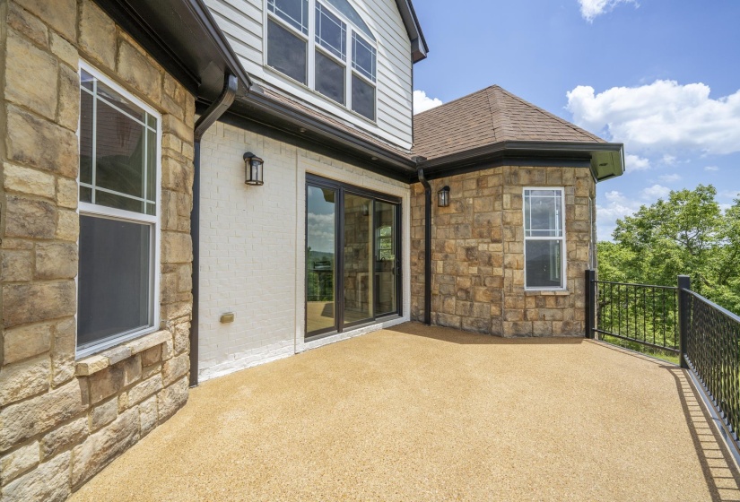 Exterior deck featuring a textured surface, black metal railing, and a stone and white brick facade