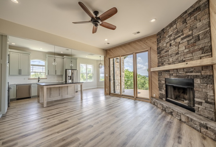 Spacious living area featuring a floor-to-ceiling stone fireplace with a wood mantel, light wood-finish flooring, and recessed lighting