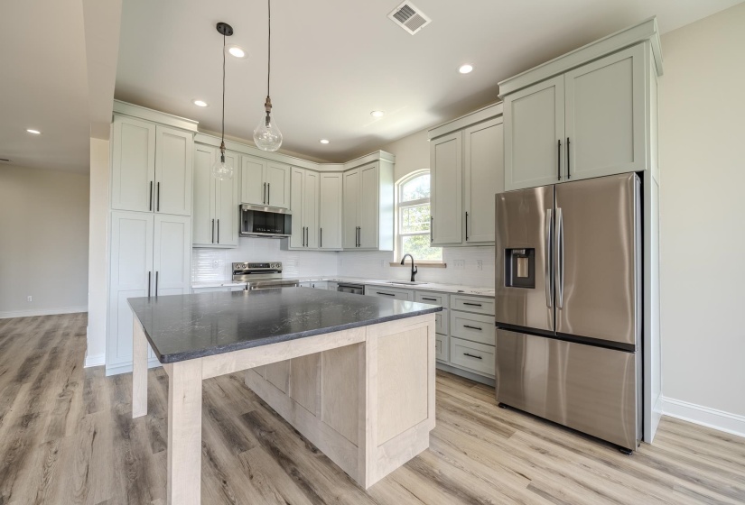 Modern kitchen featuring light-toned cabinetry, stainless steel appliances, a dark countertop kitchen island, wood-finish flooring, and recessed lighting