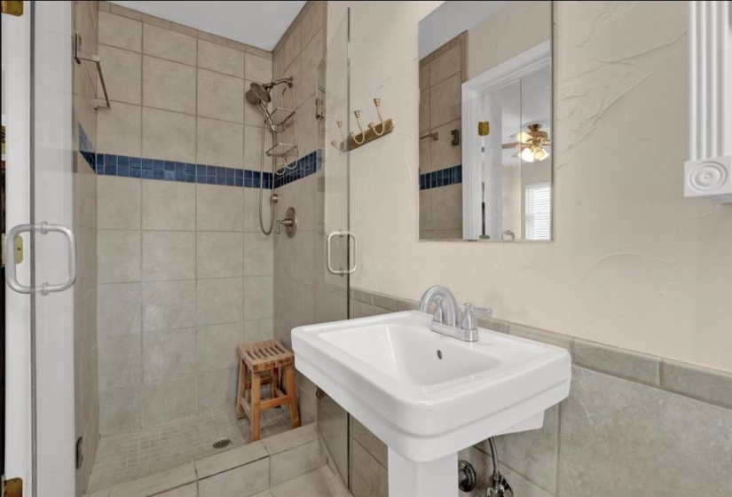 Bathroom featuring a glass-enclosed shower with tile surround and decorative blue accent, a pedestal sink with a chrome faucet, and a wall-mounted mirror