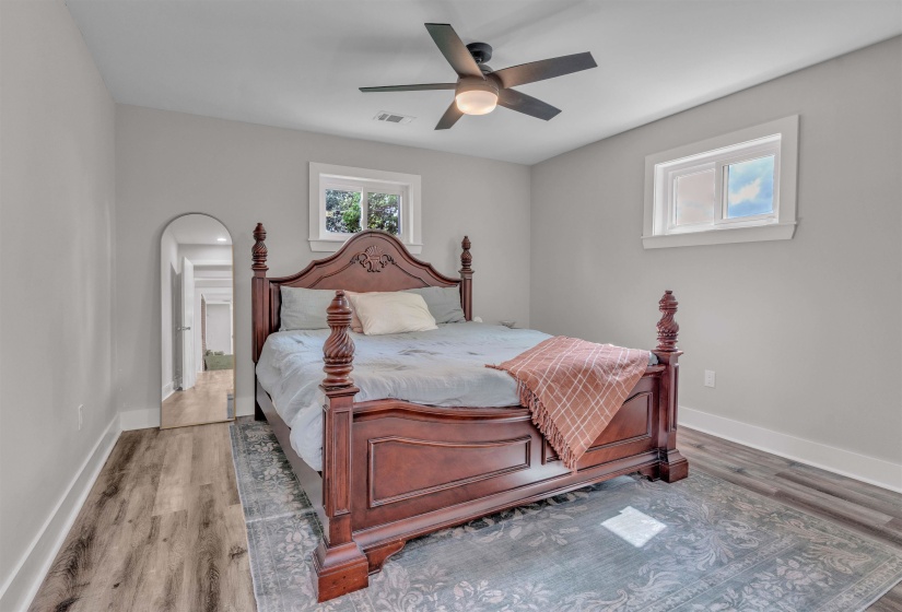 Bedroom featuring wood-finish flooring, two windows with white trim, a ceiling fan with integrated lighting, and light gray painted walls