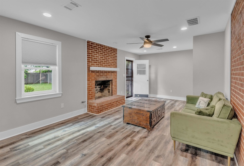 Bright living space featuring exposed brick accents, wood-finish flooring, recessed lighting, a ceiling fan, and a brick fireplace with a white mantel