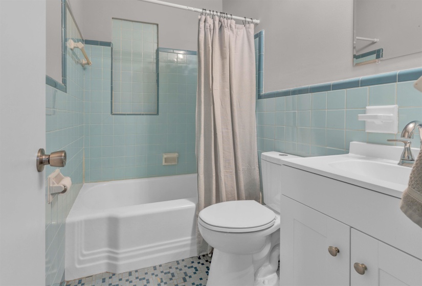 Bathroom featuring a white porcelain tub, light blue wall tiling, and mosaic floor tiling