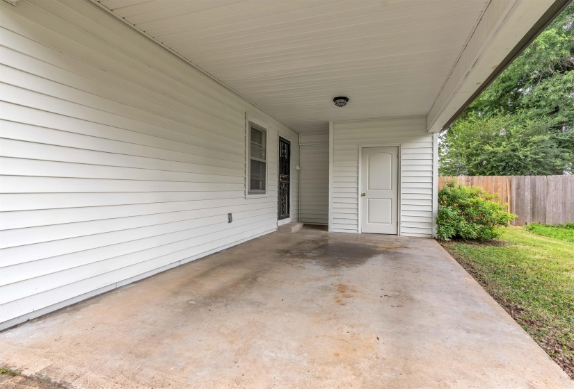 Covered concrete patio with white vinyl siding, an exterior door, a window, and a wood privacy fence