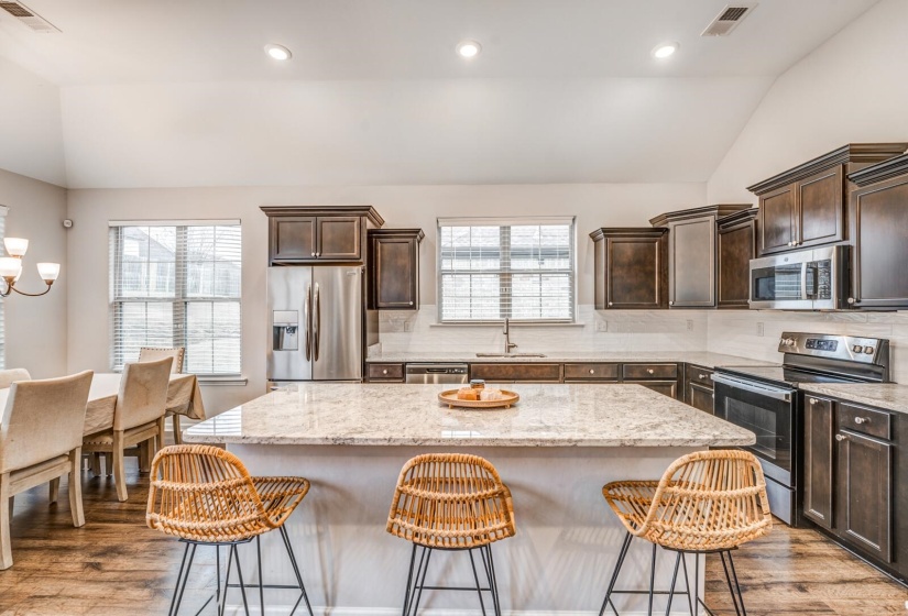 Kitchen with lofted ceiling, tasteful backsplash, dark wood finish cabinetry, stainless steel appliances, and a kitchen island