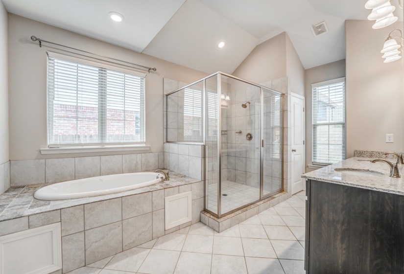 Full bathroom featuring a shower stall, double vanity, healthy amount of natural light, light tile patterned floors, and lofted ceiling
