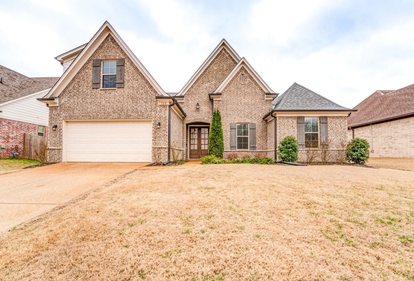 View of front of home with brick siding, french doors, concrete driveway, a front lawn, and roof with shingles