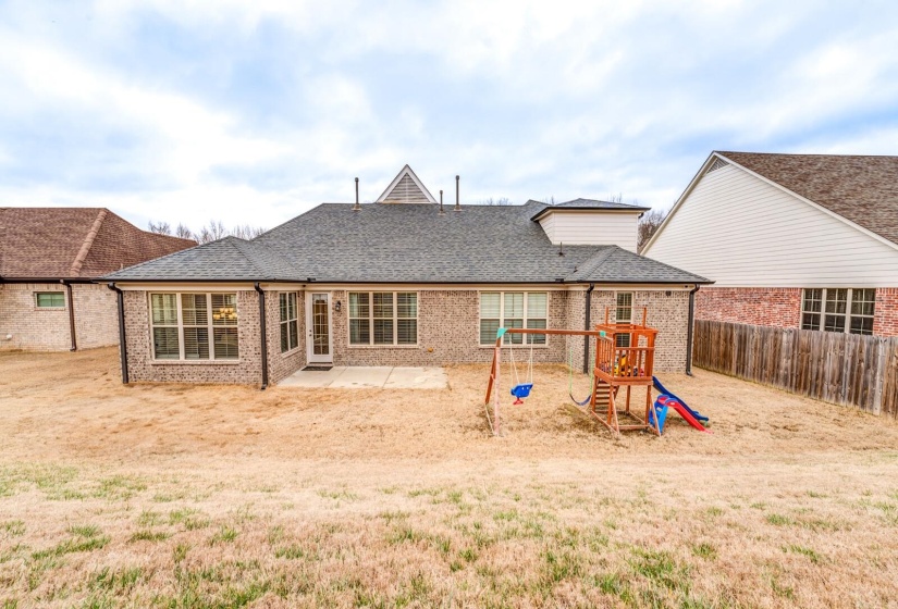 Rear view of property featuring a patio, brick siding, a shingled roof, a playground, and a fenced backyard
