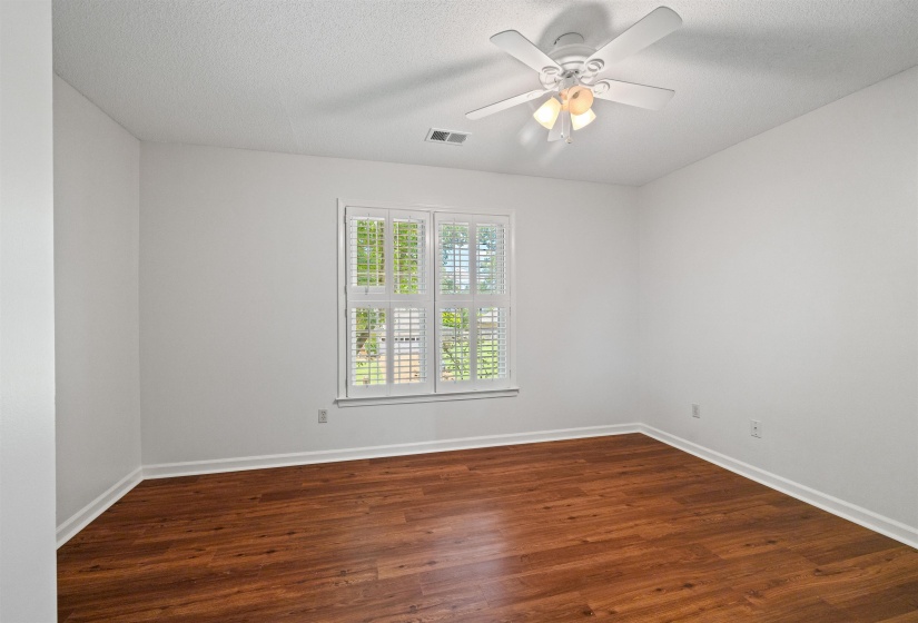 Room featuring wood-finish flooring, white baseboards, and a window with white plantation shutters