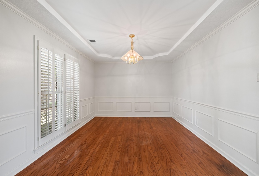 Hardwood flooring, wainscoting, and a tray ceiling with a chandelier define this room