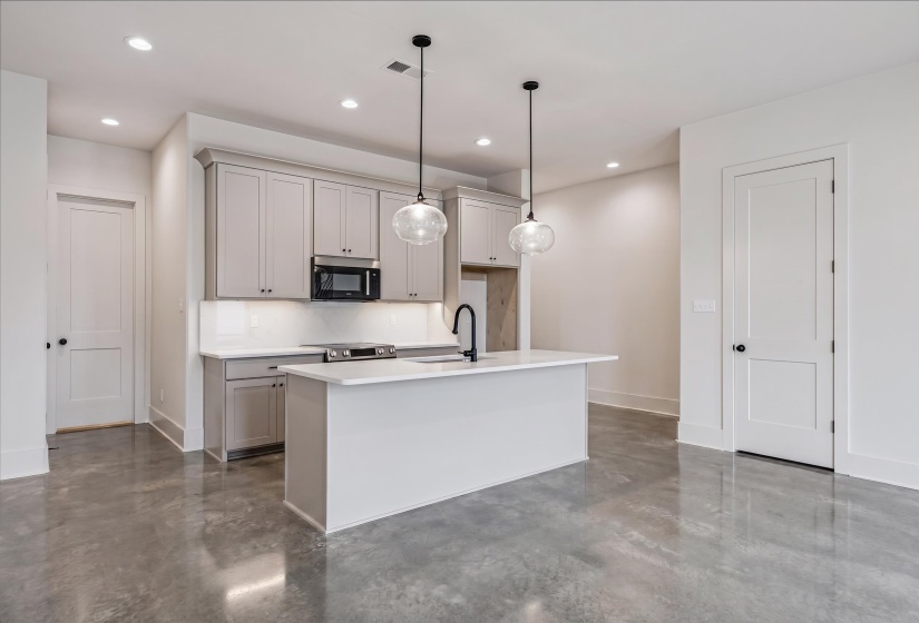 Contemporary kitchen featuring a central island, light-toned cabinetry, stainless steel appliances, pendant lighting, and polished concrete flooring