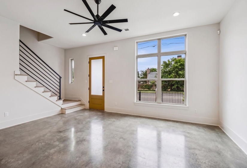 Spacious living area featuring polished concrete flooring, a modern black ceiling fan, and a prominent multi-pane window