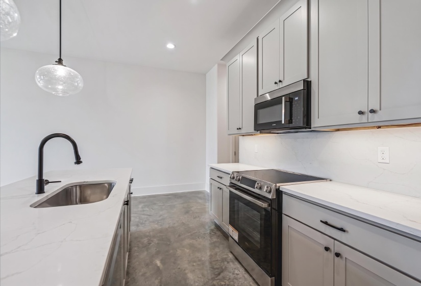 Modern kitchen featuring light gray cabinetry, stainless steel appliances, and white countertops with a matte black faucet