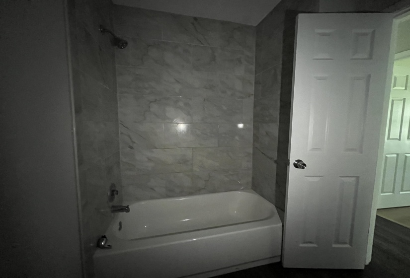 Bathroom featuring a white tub, shower with a chrome fixture, and white-veined wall tiling
