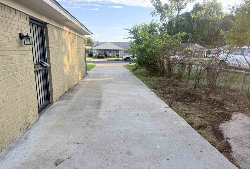 Concrete driveway and walkway bordered by a painted brick exterior and a chain-link fence