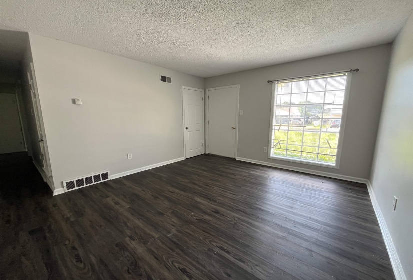 Spacious room featuring wood-finish flooring, light grey walls, white baseboards, and a large window with white muntins