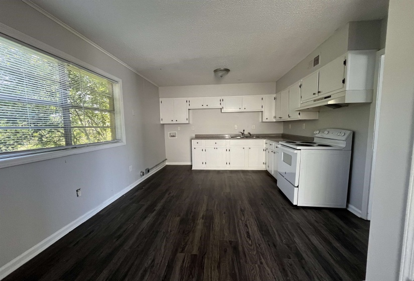 Kitchen area featuring wood-finish flooring, white cabinetry, light countertops, and a white electric range