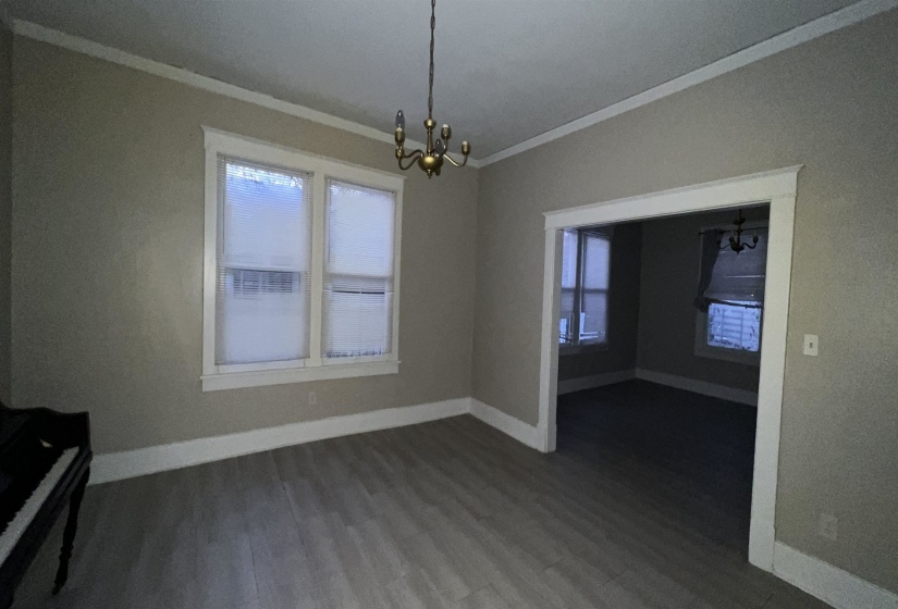 Spacious room featuring wood-finish flooring, two large windows with white trim, and a brass chandelier