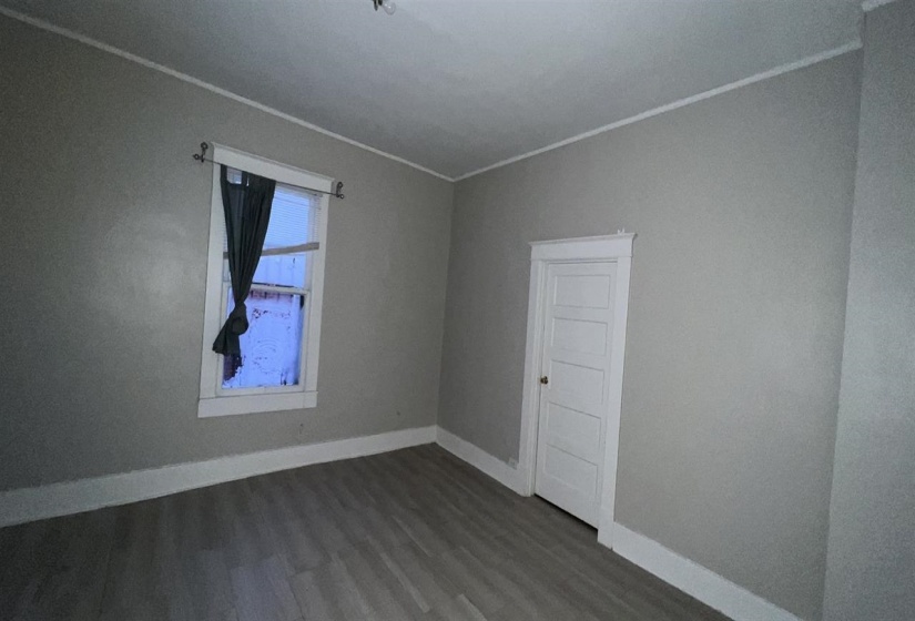 Room featuring light gray wall paint, wood-finish flooring, white baseboards, and a white five-panel door