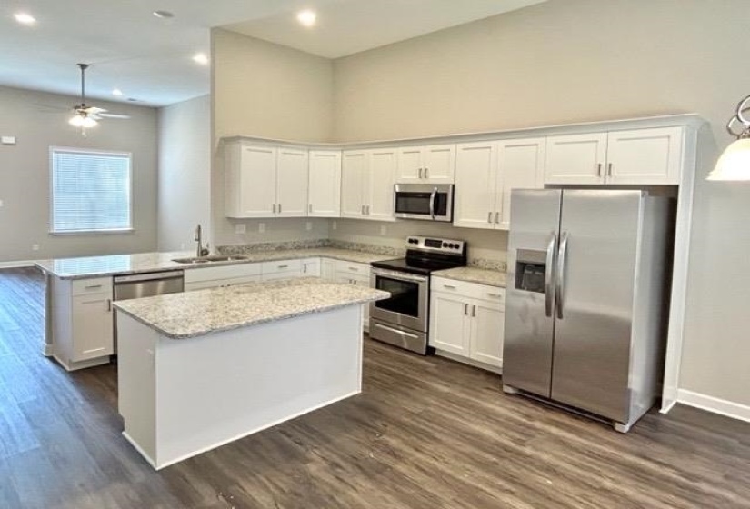 Kitchen featuring white cabinetry, stainless steel appliances, speckled countertops, a central island, and wood-finish flooring