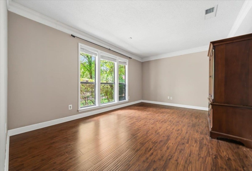 Spacious interior room featuring wood-finish flooring, a neutral wall palette, and crown molding