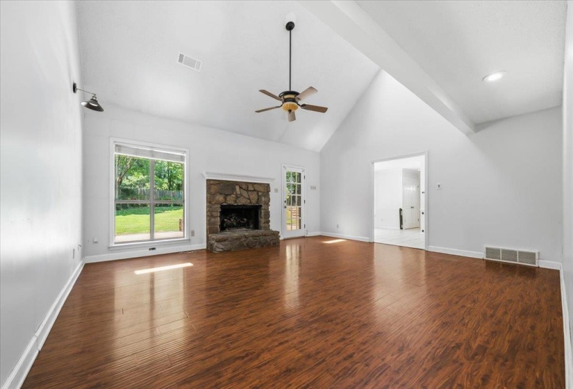 Spacious living area featuring vaulted ceilings, wood-finish flooring, a stone fireplace, and an exterior glass-paneled door