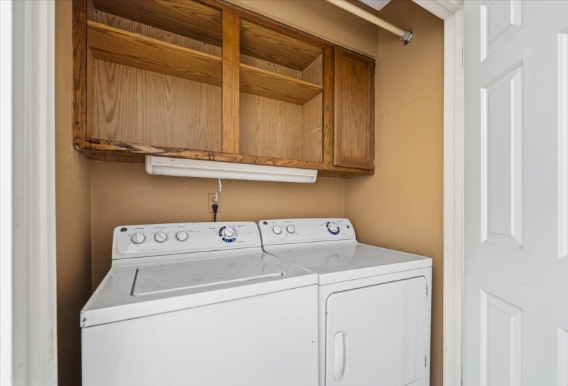 Dedicated laundry area featuring wood-finish cabinetry with open shelving and closed storage