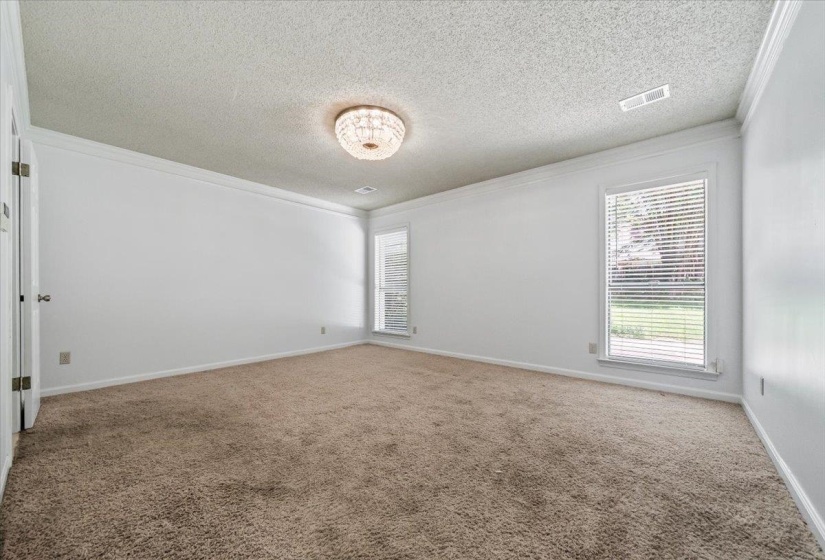 Spacious room featuring carpeted flooring, two windows with blinds, a crystal-style flush mount light fixture, and crown molding