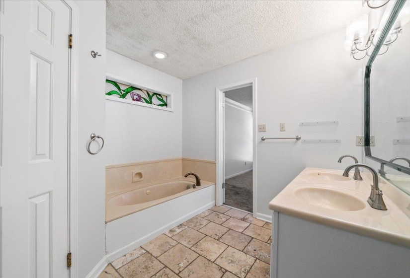 Bathroom featuring a built-in tub, dual sink vanity, tiled flooring, recessed lighting, and a decorative stained glass window